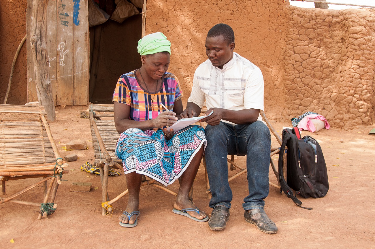 A female member of our project in Mali sat with a Tree Aid partner staff member outside her house, filling in a form