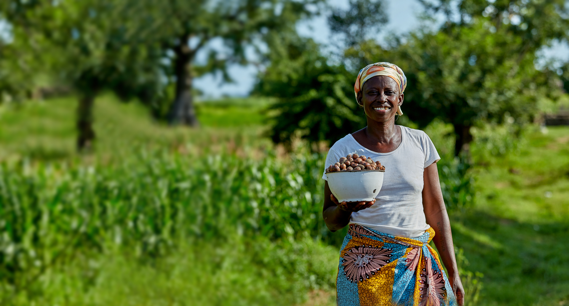 A woman smiling and holding a bowl of shea nuts she has collected.