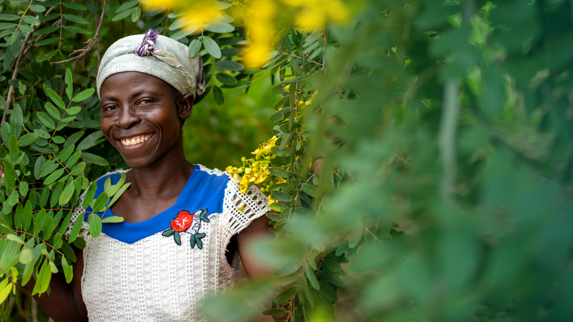 Abba Achana smiling as her portrait is taken against a leafy backdrop, © 2021 Tree Aid.