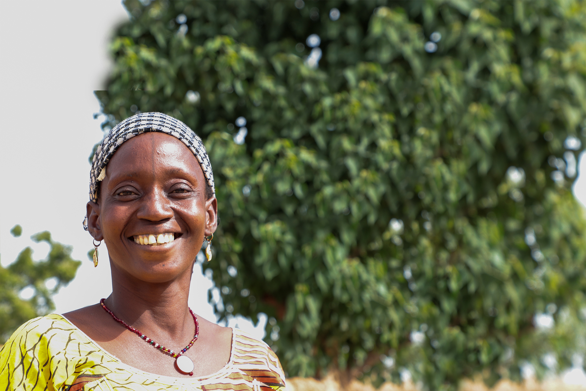 Djamako, a woman on Tree Aid's She Grows project, smiling in front of trees.