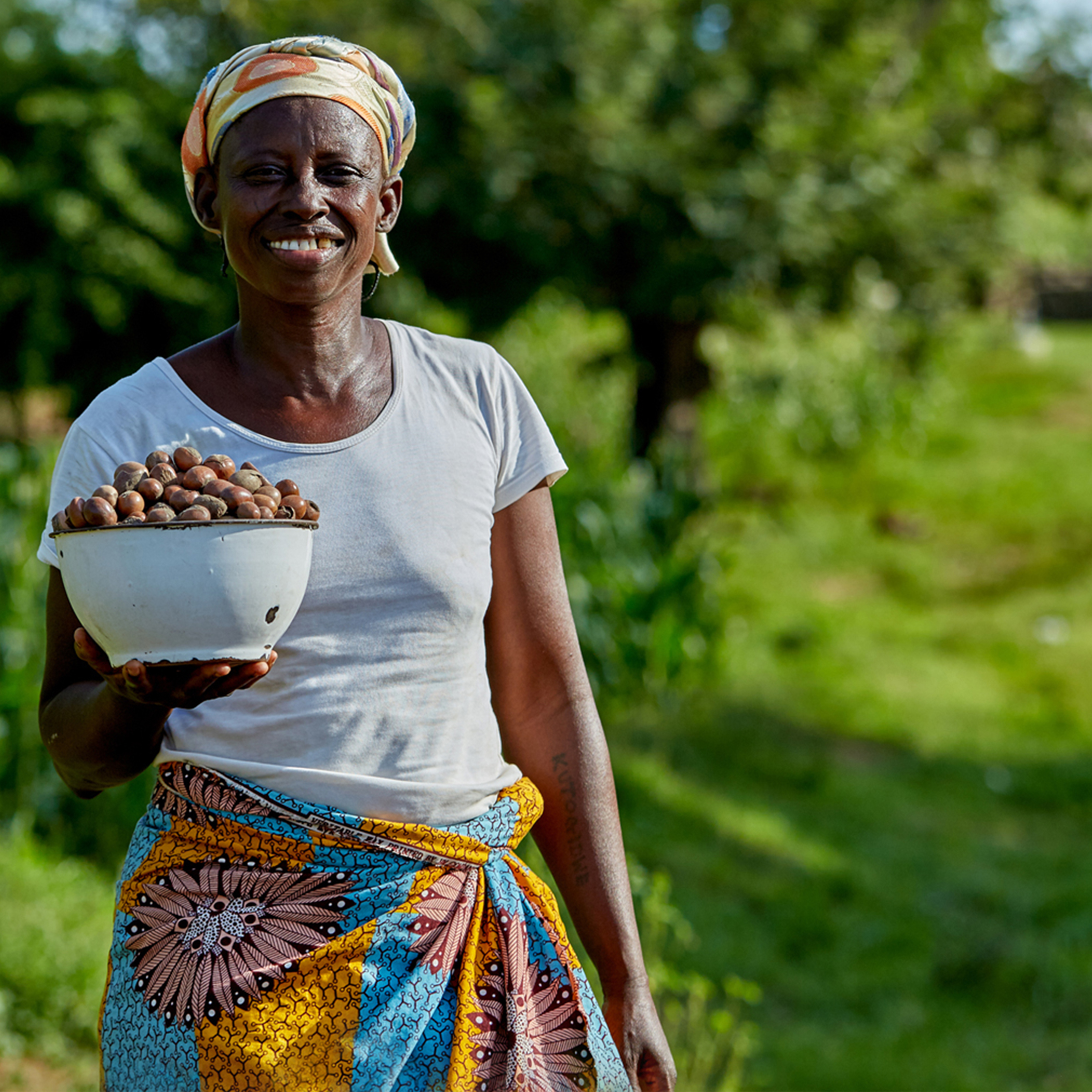 A women smiling and holding a bowl of shea nuts.