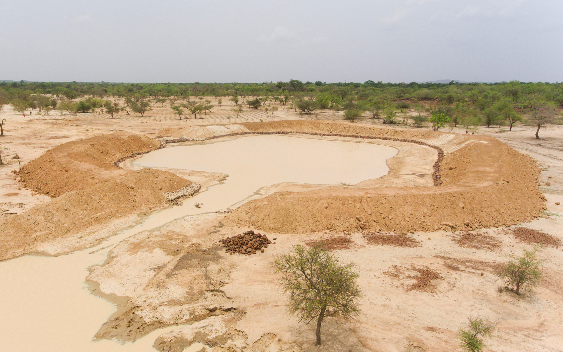 An aerial shot of a large pit of water in the land surrounded by trees - this is a boulis.