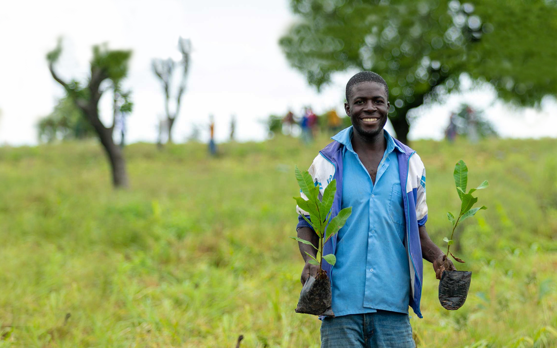 Francis, a man we are working with in Ghana, holding a tree sapling in each hand which he will plant in the community.