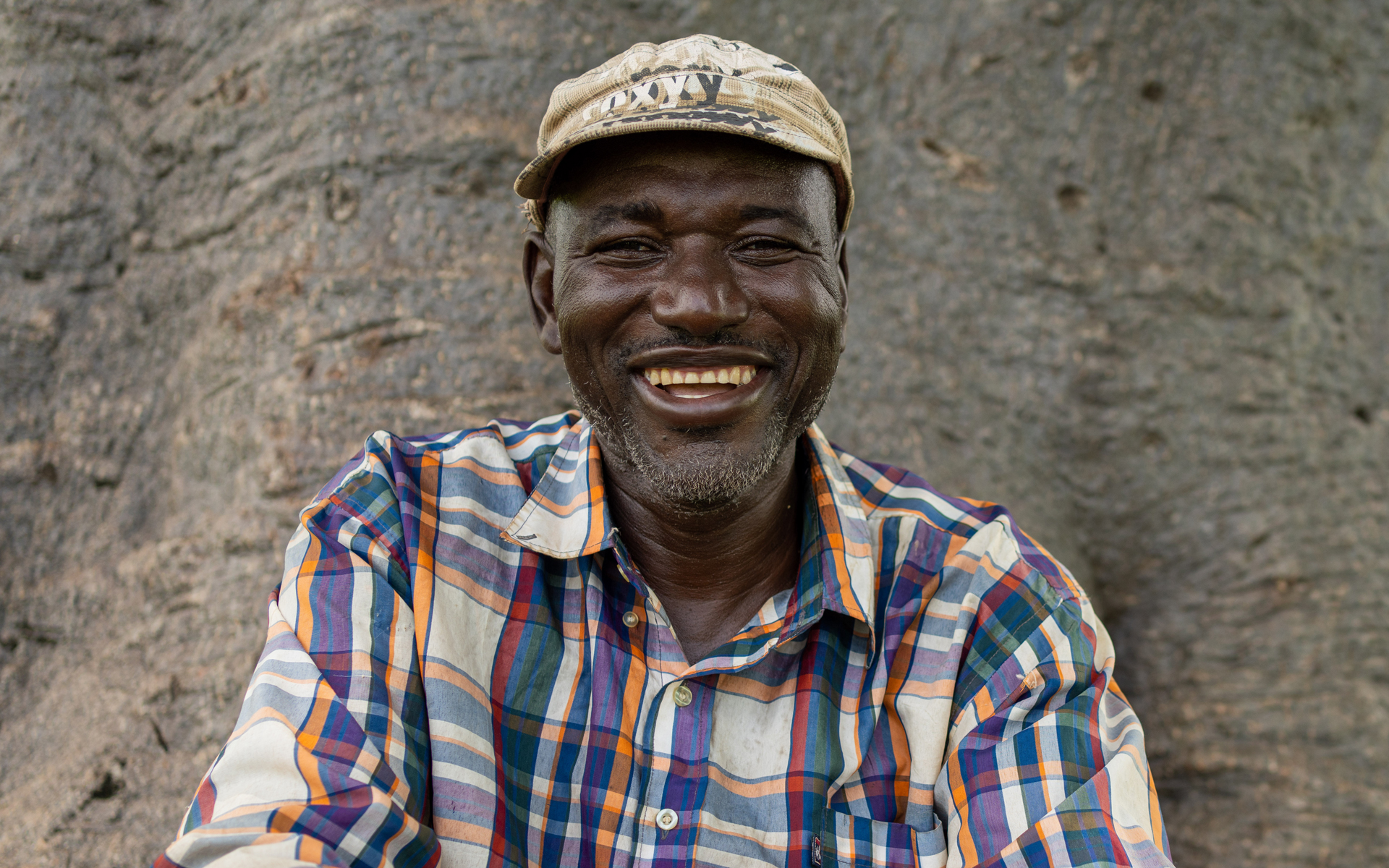 Close up shot of Baata Awujani smiling sitting on a tree trunk, © 2021 Tree Aid.
