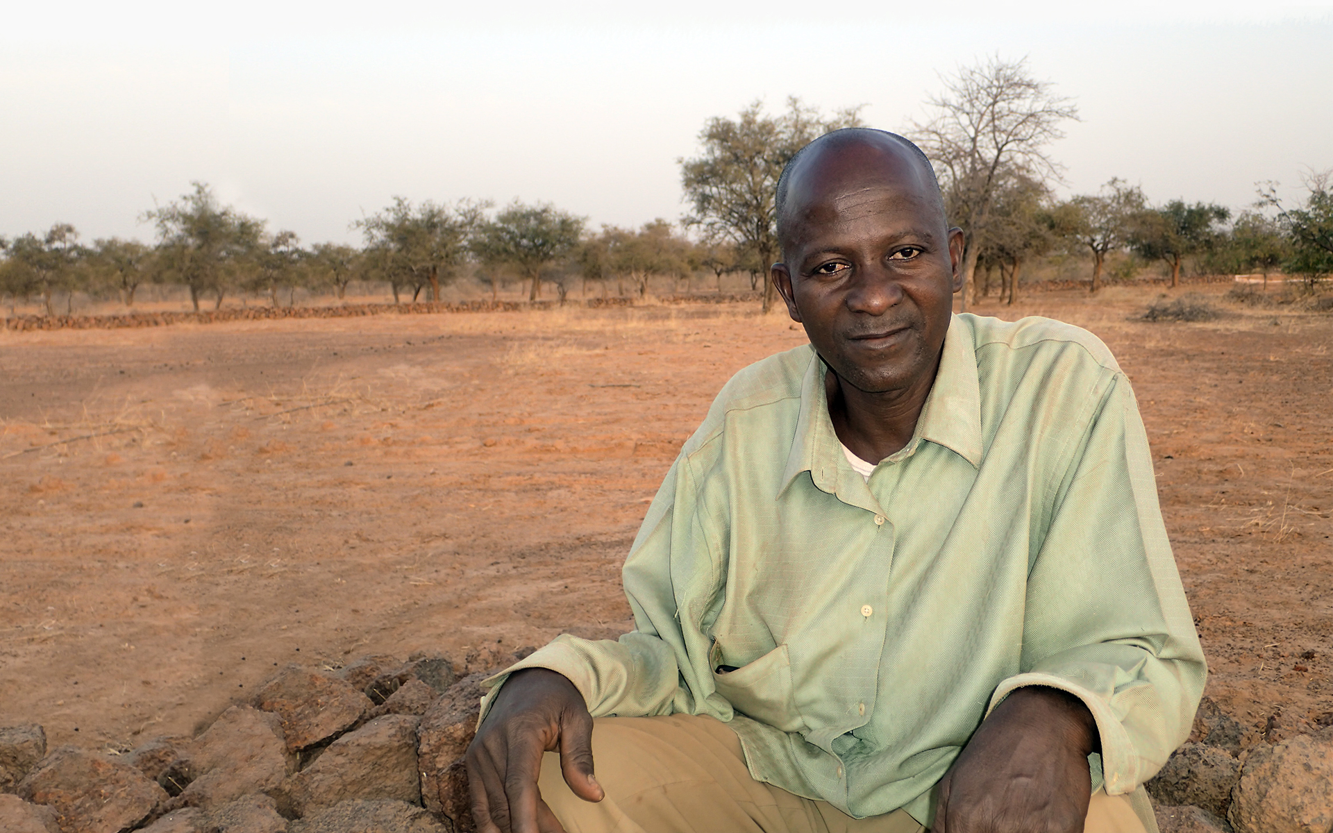 Amade, a man in Burkina Faso that Tree Aid worked with, sitting in front of a degraded landscape. 