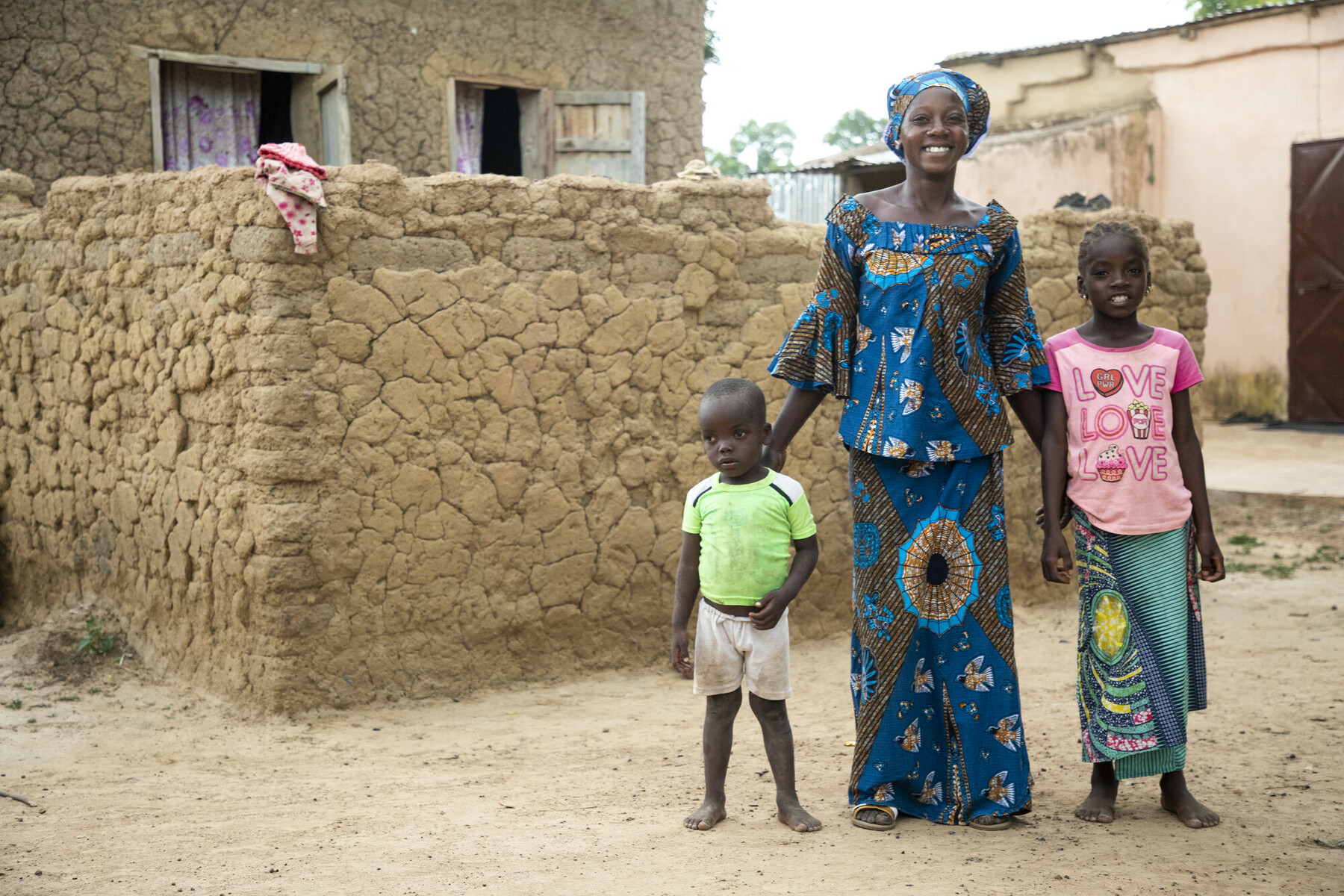 Portrait of Sekoura Diarra stood outside her house with her two young children